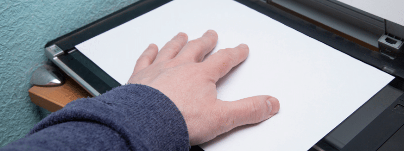 A hand placed on a piece of paper in a paper scanner